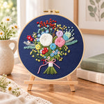 Navy floral bouquet embroidery kit finished hoop displayed on a wooden stand as cozy tabletop decor