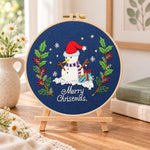 Navy snowman art embroidery kit finished hoop displayed on a wooden stand as cozy tabletop decor