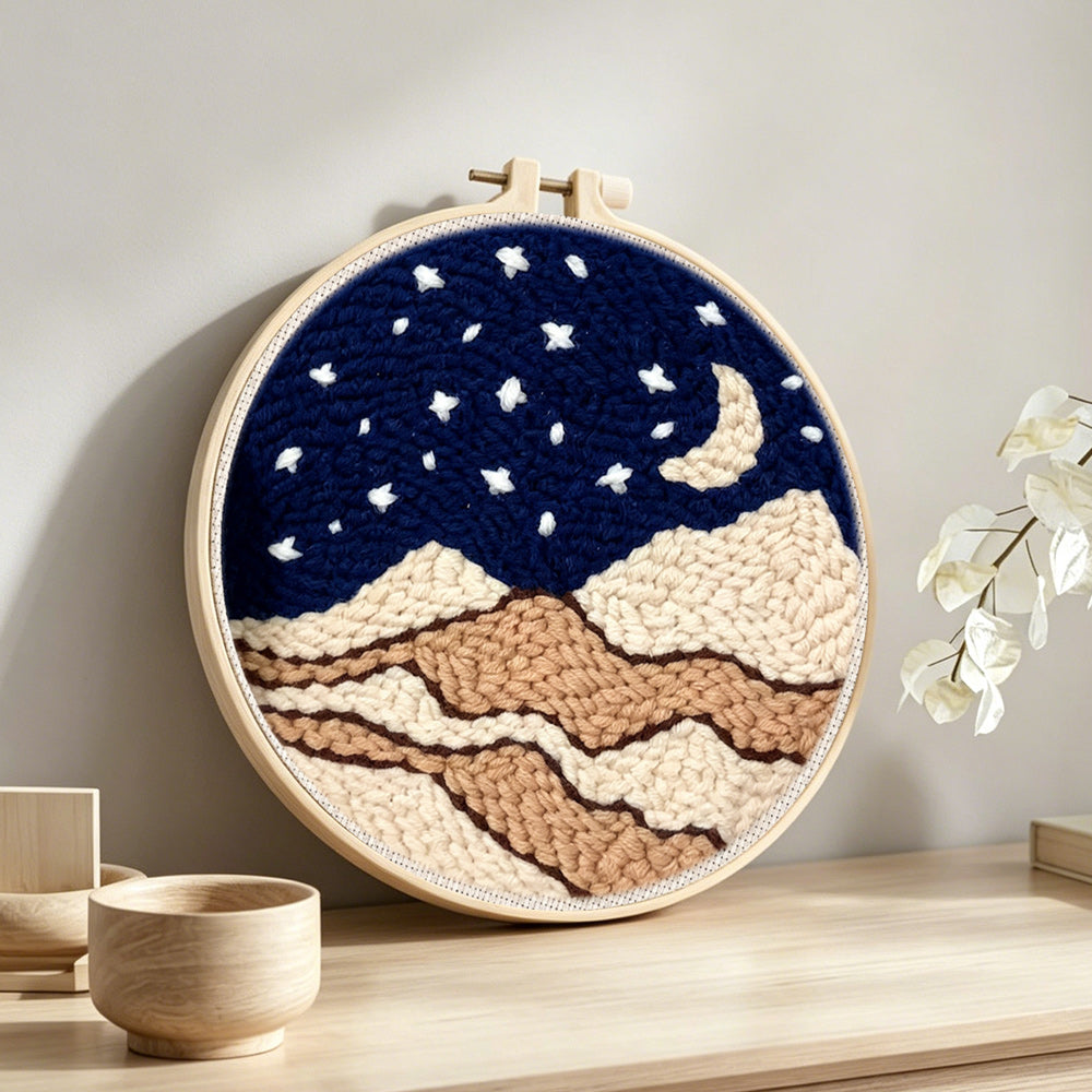 Night sky with moon, stars and beige sand dunes punch needle artwork displayed on a table