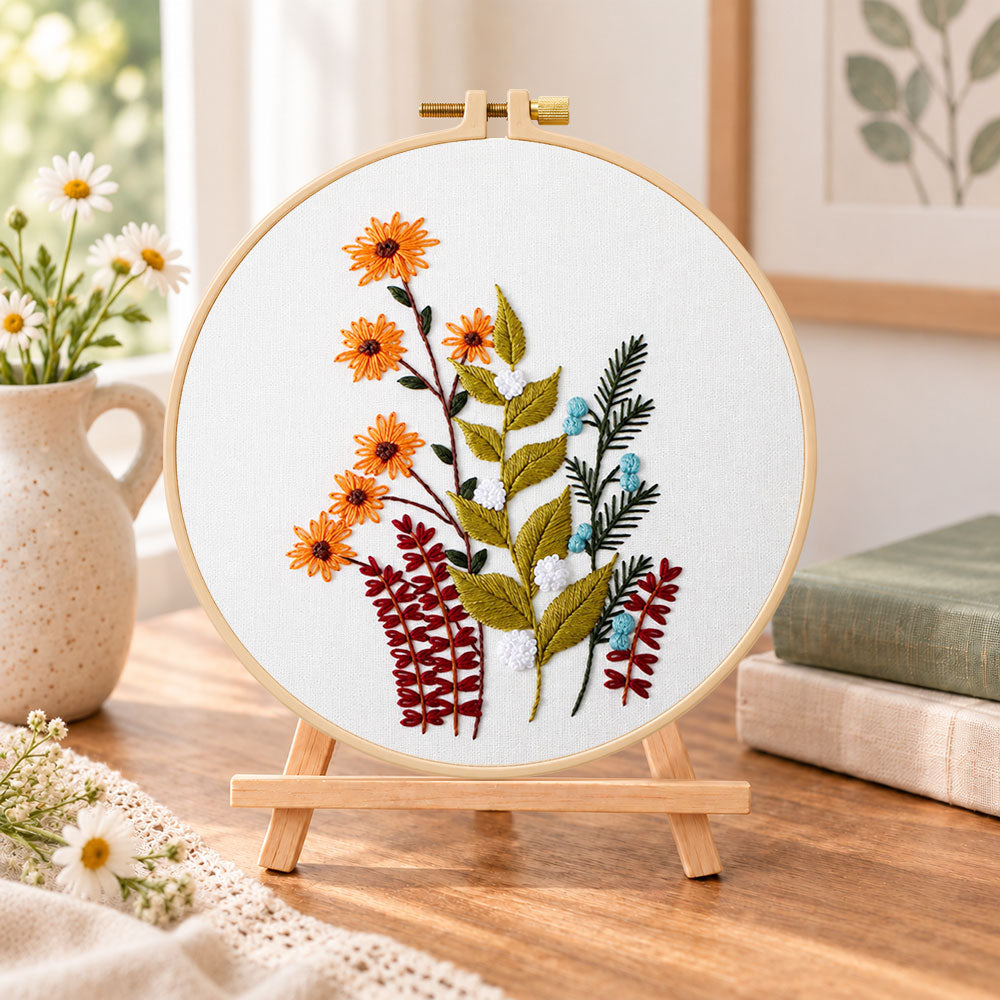 Orange daisy floral sprig embroidery kit finished hoop displayed on a wooden stand as cozy tabletop decor
