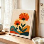 Orange flowers and radiant sunset punch needle artwork displayed on a table