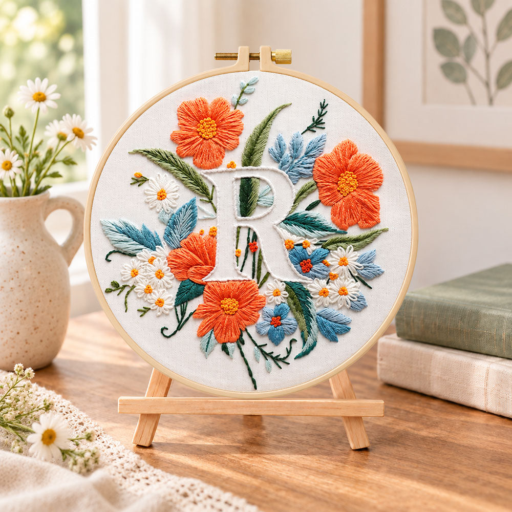 Orange poppies and letter r embroidery kit finished hoop displayed on a wooden stand as cozy tabletop decor