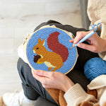 Creating handmade orange squirrel holding pine cone punch needle artwork