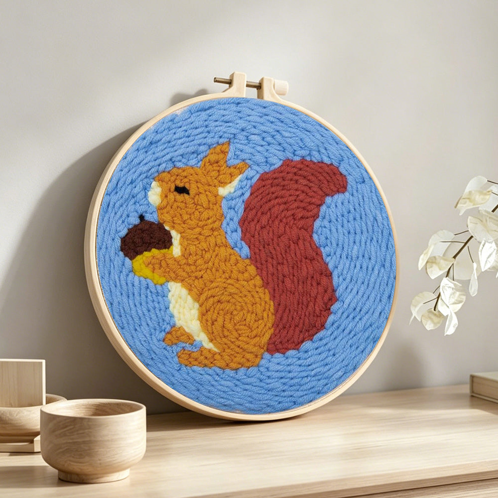Orange squirrel holding pine cone punch needle artwork displayed on a table