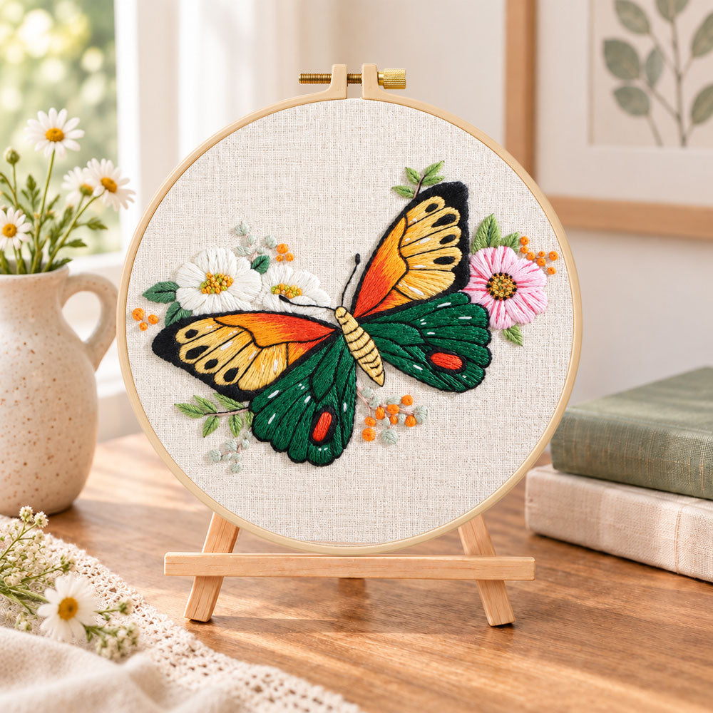 Orange‑winged butterfly embroidery kit finished hoop displayed on a wooden stand as cozy tabletop decor