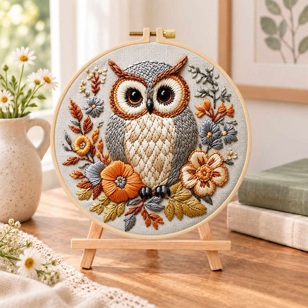 Owl among autumn blooms embroidery kit finished hoop displayed on a wooden stand as cozy tabletop decor