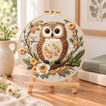 Owl on blossom branch embroidery kit finished hoop displayed on a wooden stand as cozy tabletop decor