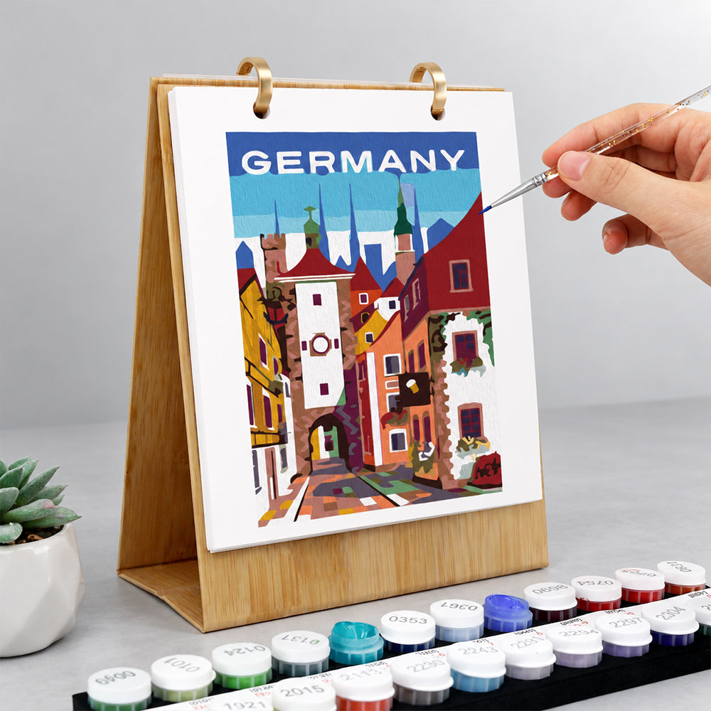 Hand adding finishing details to a German old town painting on a wooden desk calendar