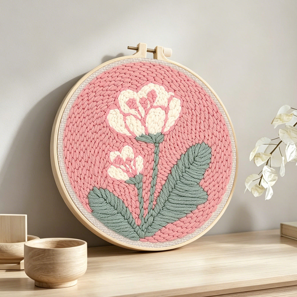 Pale pink background with white flowers punch needle artwork displayed on a table