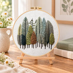 Pastel forest grove embroidery kit finished hoop displayed on a wooden stand as cozy tabletop decor