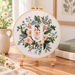 Pastel pink blooms and letter u embroidery kit finished hoop displayed on a wooden stand as cozy tabletop decor