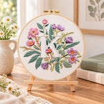 Pink blooms and letter k embroidery kit finished hoop displayed on a wooden stand as cozy tabletop decor