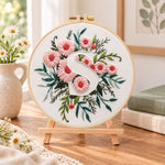 Pink daisy blooms and letter s embroidery kit finished hoop displayed on a wooden stand as cozy tabletop decor
