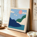 Pink sun and green hills punch needle artwork displayed on a table