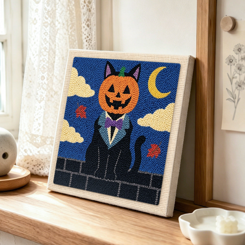Pumpkin‑headed black cat punch needle artwork displayed on a table