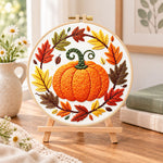 Pumpkin wreath with fall foliage embroidery kit finished hoop displayed on a wooden stand as cozy tabletop decor