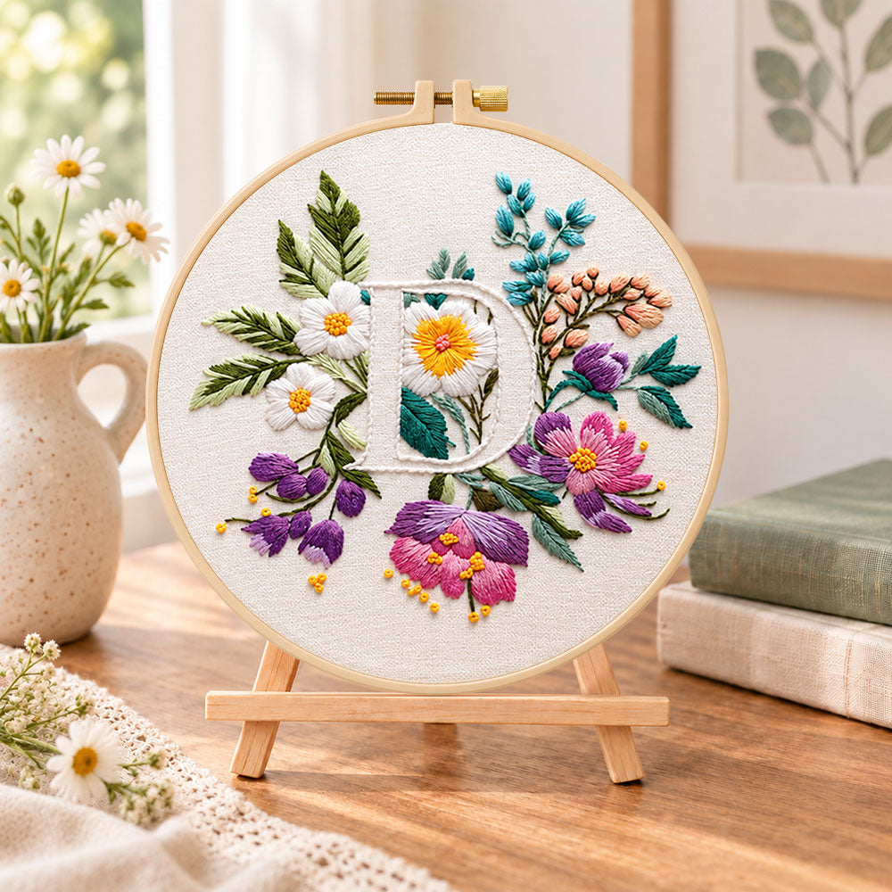 Purple daisy garden and letter d embroidery kit finished hoop displayed on a wooden stand as cozy tabletop decor