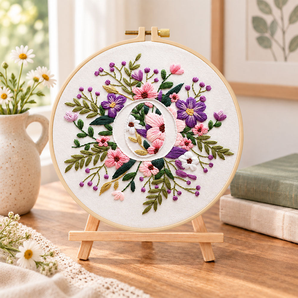 Purple floral ring and letter o embroidery kit finished hoop displayed on a wooden stand as cozy tabletop decor