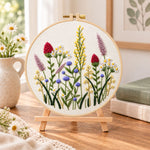 Purple meadow wildflower embroidery kit finished hoop displayed on a wooden stand as cozy tabletop decor