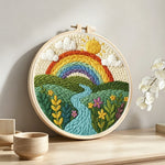 Rainbow over the rolling river and green fields punch needle artwork displayed on a table
