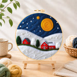 Finished red barns under the giant golden moon needle felting displayed on a wooden easel