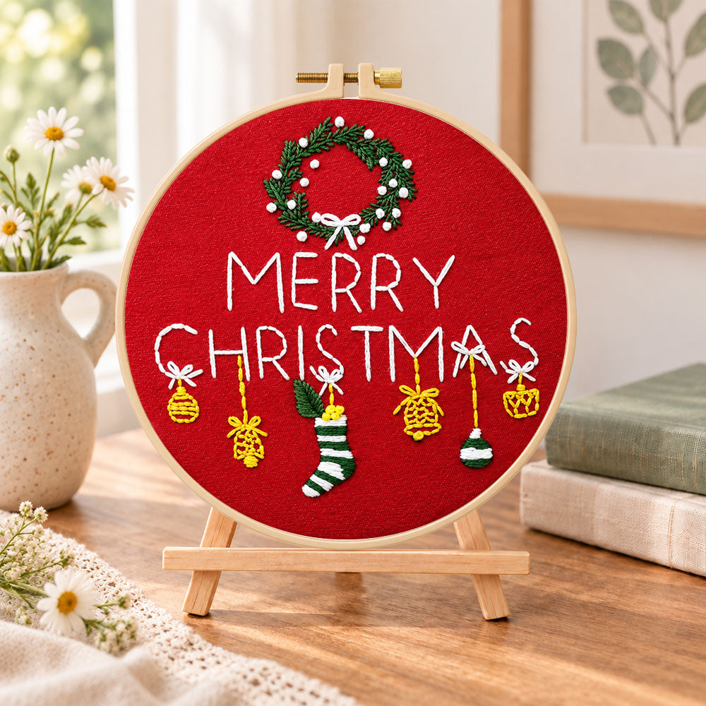 Red christmas greeting embroidery kit finished hoop displayed on a wooden stand as cozy tabletop decor