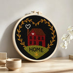 Red house with “home” heart wreath punch needle artwork displayed on a table