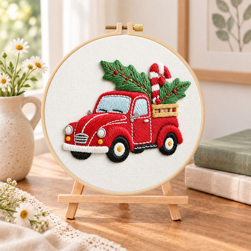 Red pick‑up with holly embroidery kit finished hoop displayed on a wooden stand as cozy tabletop decor