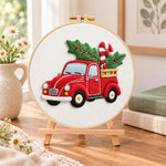 Red pick‑up with holly embroidery kit finished hoop displayed on a wooden stand as cozy tabletop decor