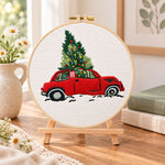Red truck christmas tree embroidery kit finished hoop displayed on a wooden stand as cozy tabletop decor