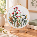 Red wildflower bouquet embroidery kit finished hoop displayed on a wooden stand as cozy tabletop decor