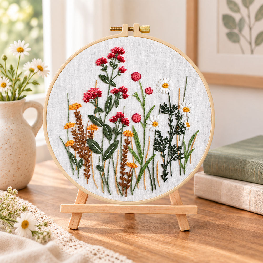 Red wildflower bouquet embroidery kit finished hoop displayed on a wooden stand as cozy tabletop decor
