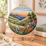 Rolling hills floral vista embroidery kit finished hoop displayed on a wooden stand as cozy tabletop decor