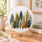 Rustic pine tree grove embroidery kit finished hoop displayed on a wooden stand as cozy tabletop decor