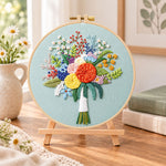 Sage green floral bouquet embroidery kit finished hoop displayed on a wooden stand as cozy tabletop decor