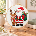 Santa and reindeer companions embroidery kit finished hoop displayed on a wooden stand as cozy tabletop decor