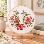 Scarlet florals and letter t embroidery kit finished hoop displayed on a wooden stand as cozy tabletop decor