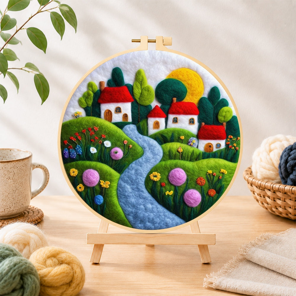 Finished serene blue river and red roof village needle felting displayed on a wooden easel