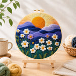 Finished serene mountain sunset and white daisies needle felting displayed on a wooden easel