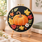 Single pumpkin on black fabric embroidery kit finished hoop displayed on a wooden stand as cozy tabletop decor