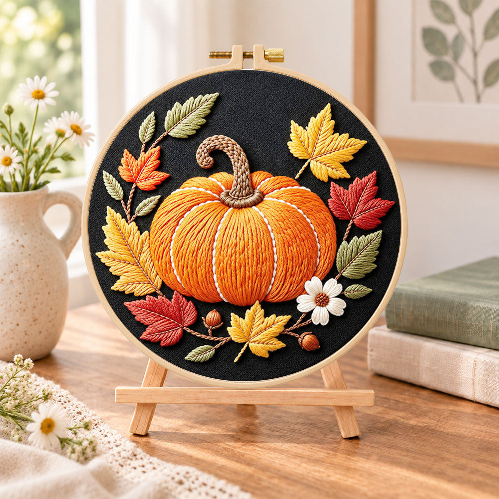 Single pumpkin on black fabric embroidery kit finished hoop displayed on a wooden stand as cozy tabletop decor