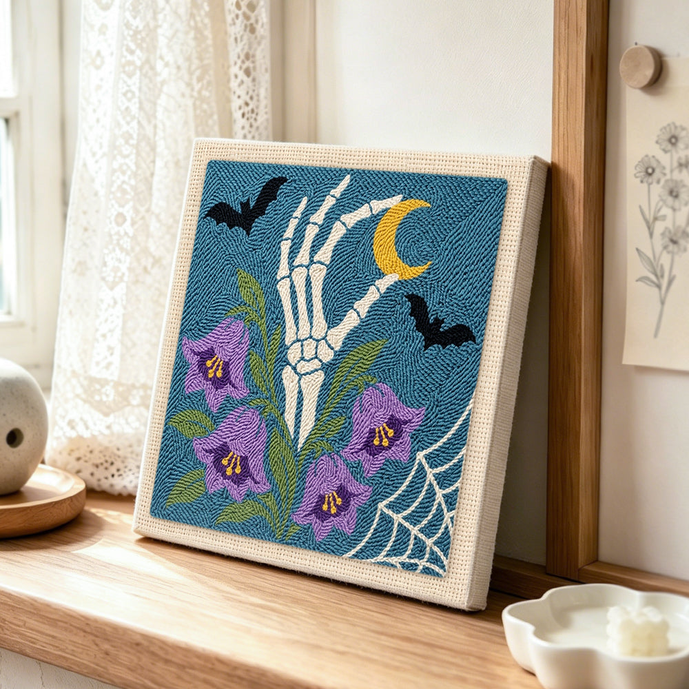 Skeleton hand with purple bellflowers punch needle artwork displayed on a table
