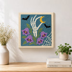 Finished skeleton hand with purple bellflowers artwork displayed on a wall