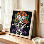 Skeleton hands holding roses punch needle artwork displayed on a table