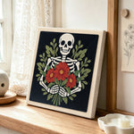 Skeleton holding red blooms punch needle artwork displayed on a table