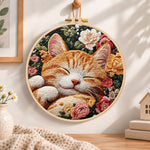 Sleeping ginger cat among roses embroidery hoop wall art displayed as warm and cozy handmade home decor