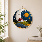 Smiling giant moon and little red cottage needle felt wall art displayed in a bright home interior