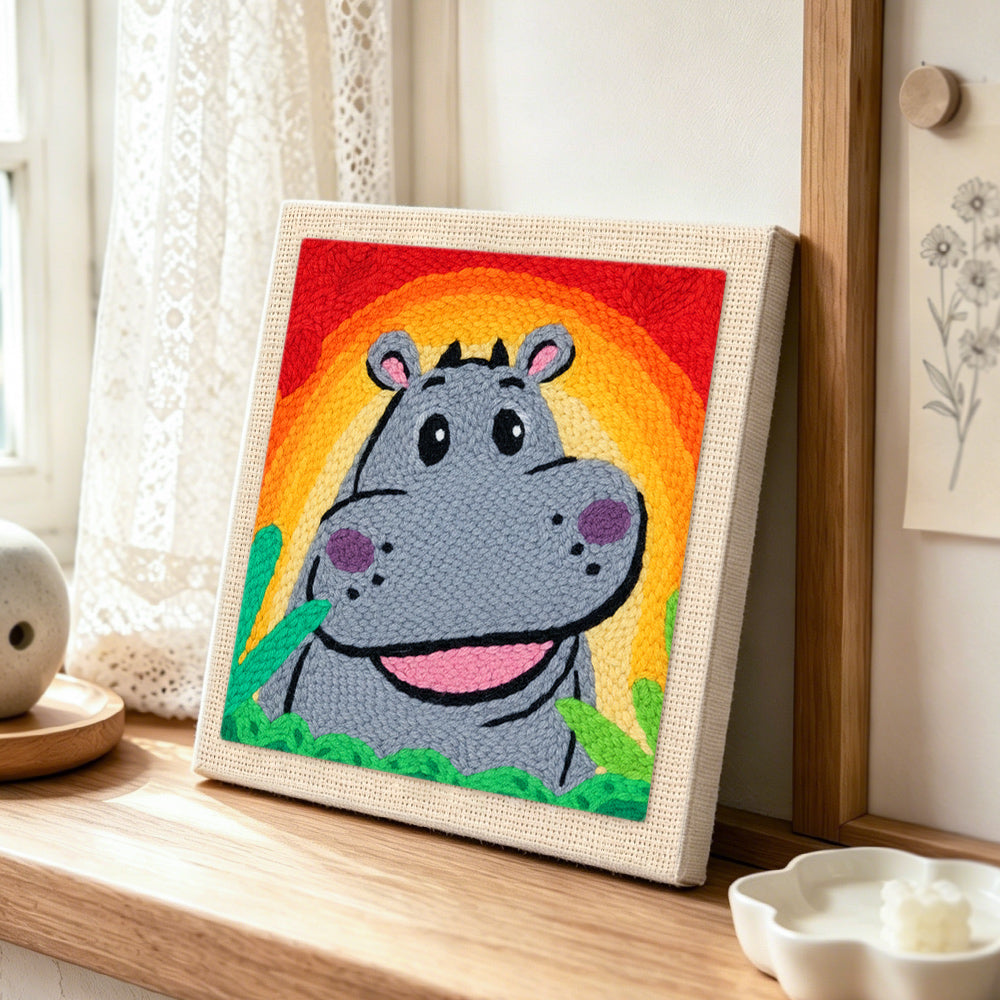 Smiling gray hippo with rainbow sunset punch needle artwork displayed on a table
