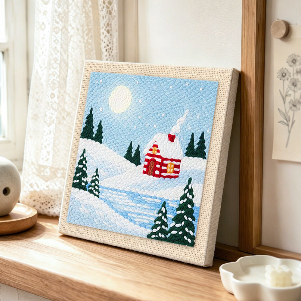 Snow cabin in moonlight punch needle artwork displayed on a table