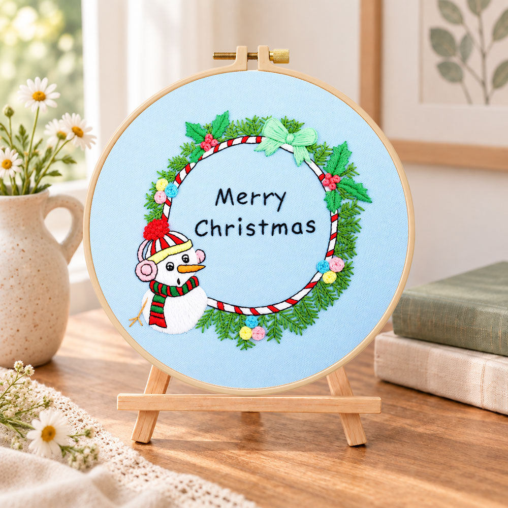 Snowman wreath quote embroidery kit finished hoop displayed on a wooden stand as cozy tabletop decor